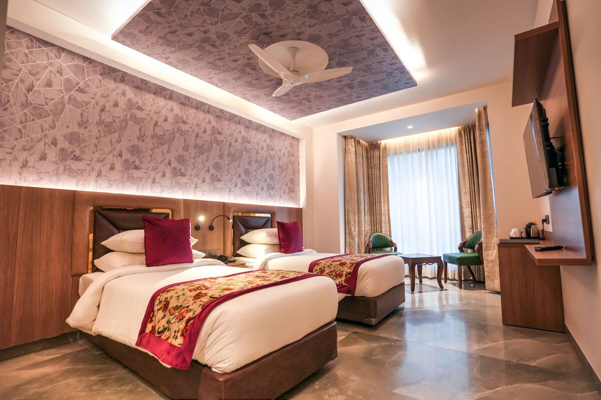 A hotel room with two beds, a ceiling fan, a TV, and a desk with a chair.
