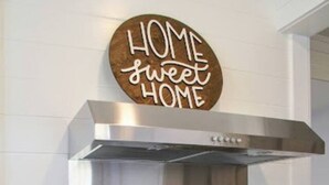 A kitchen with a stainless steel range hood, a black stove, and a pot on the stove. There is a knife block on the counter and a bottle of olive oil. A sign above the stove reads "HOME sweet HOME". - Mall St · Cozy Haven In The City W/Deck <5 min to DT Knox (Knoxville)