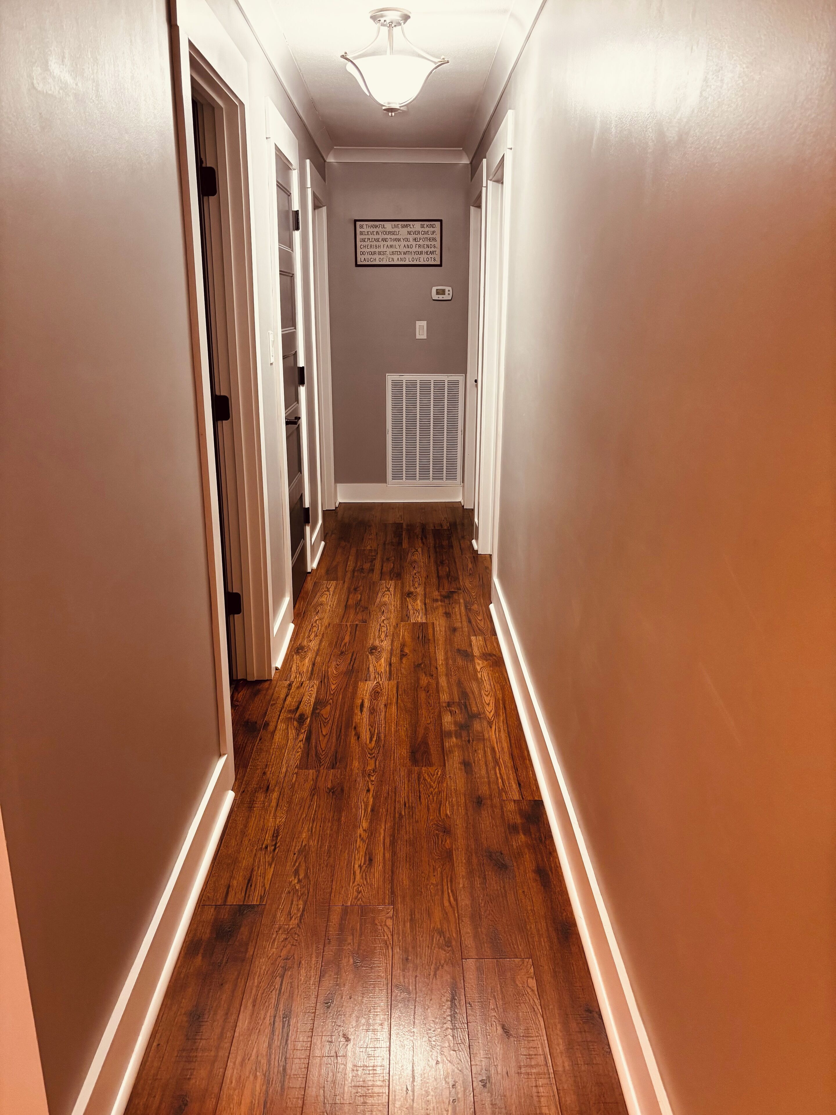 Un couloir doté d’un plancher en bois, de murs blancs et d’un luminaire au plafond.