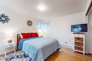 A bedroom with a bed, red pillows, a TV on a stand, a nightstand, and a wall with decorative elements.