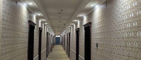 A long, narrow hotel corridor with doors on both sides, a patterned carpet, and overhead lighting.