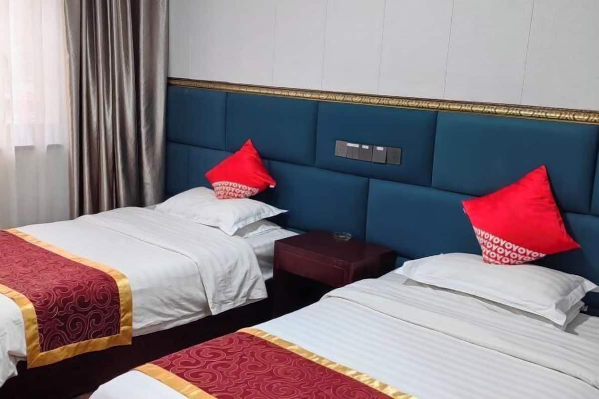 A hotel room with two beds, each with a red pillow, a nightstand, and a wall-mounted control panel.