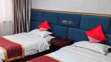 A hotel room with two beds, each with a red pillow, a nightstand, and a wall-mounted control panel.