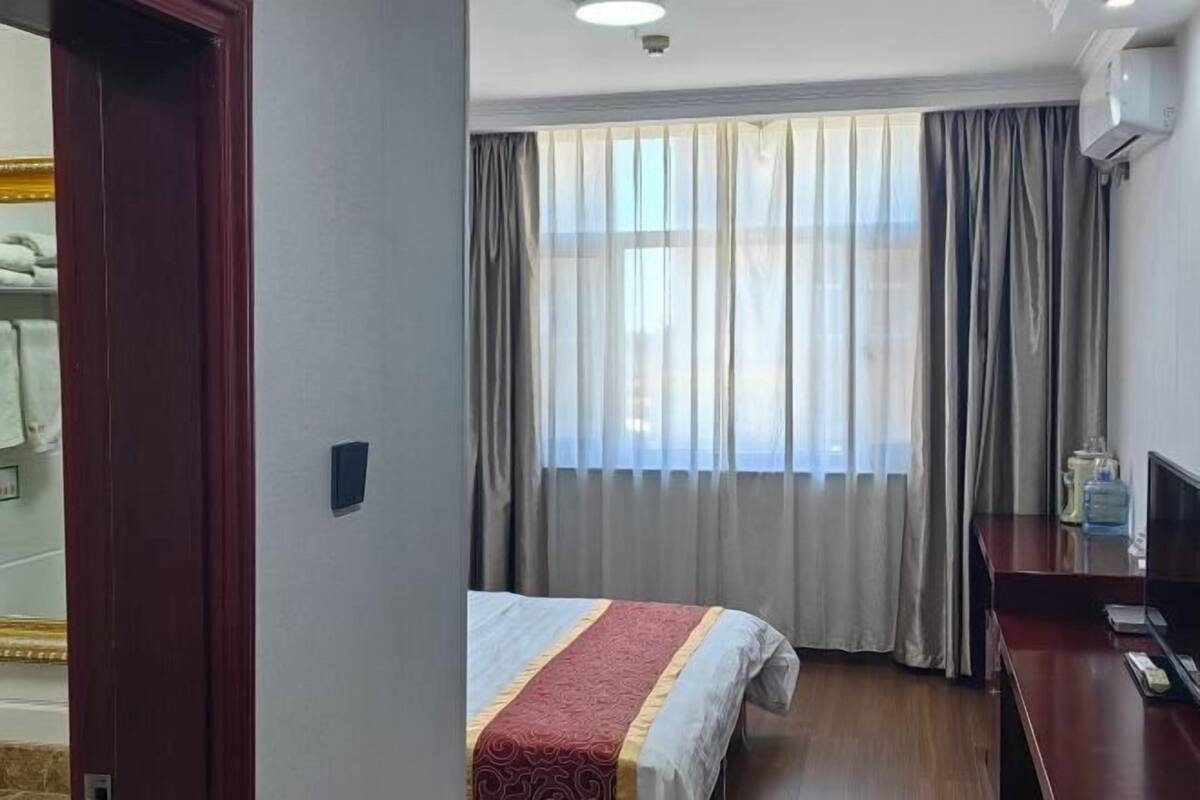 A hotel room with a bed, a television, a desk, and a window with curtains.