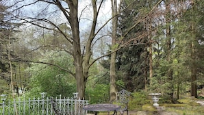 Un jardí amb una taula i cadires metàl·liques, envoltat d'una tanca de metall blanc i arbres.