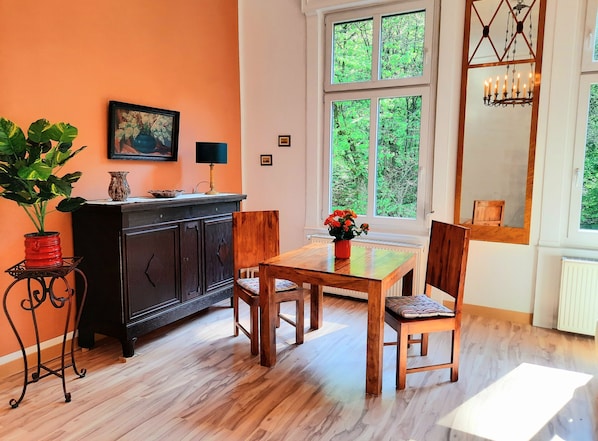 Un comedor con una mesa y sillas de madera, un armario negro, una planta en maceta y un ventanal con vista a follaje.