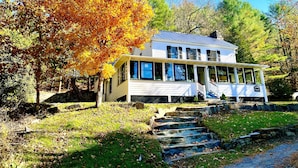 Une maison blanche dotée d’un porche, entourée d’arbres aux feuilles d’automne.