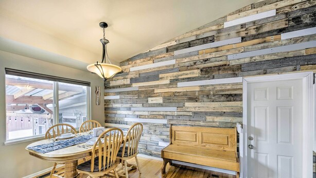 Un comedor con una mesa y sillas de madera, un banco, una lámpara colgante y una pared de madera rústica.