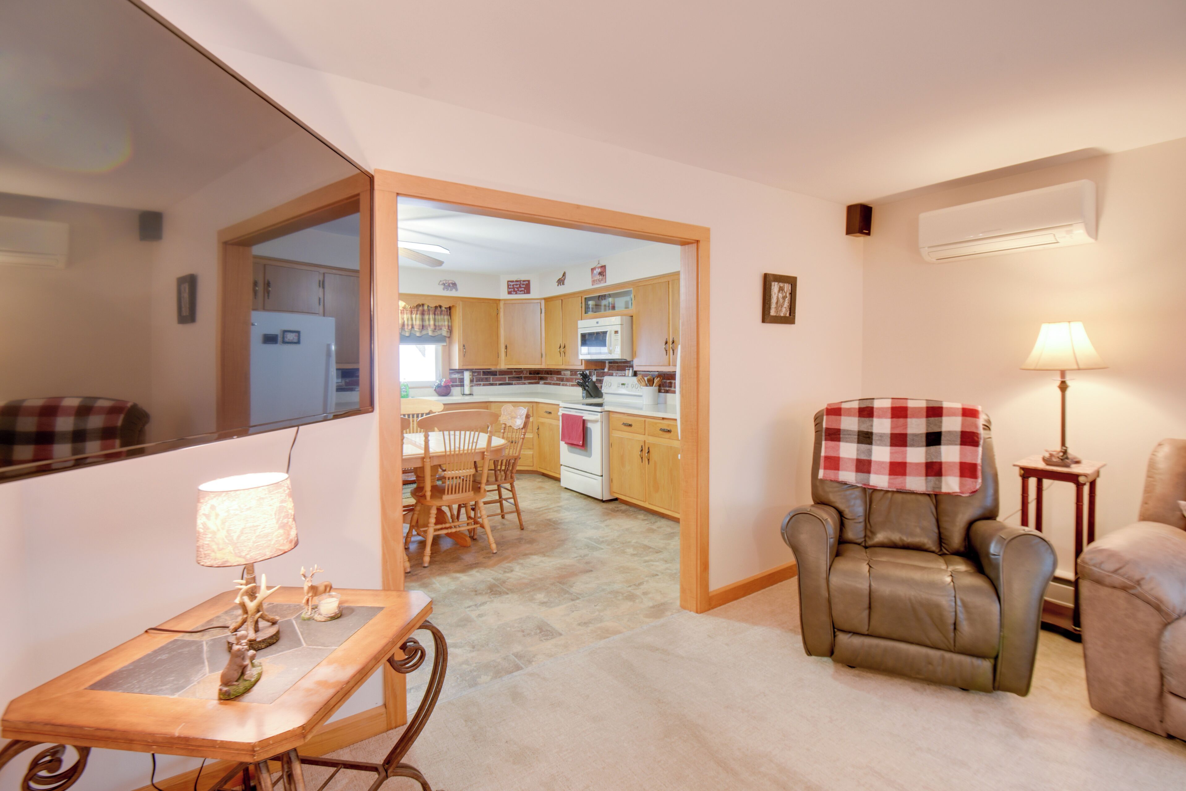 Een woonkamer met een bank, een fauteuil, een tafel met een lamp en uitzicht op de keuken.