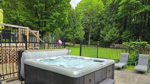 A hot tub in a backyard with a wooden deck, a metal fence, and a grassy area with trees. - Enjoy Orleans Island at Residence Orleans with it magnificent inground pool (Sainte-Pétronille)