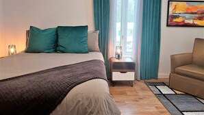 A bedroom with a bed, a nightstand, a chair, and a painting on the wall. - Enjoy Orleans Island at Residence Orleans with it magnificent inground pool (Sainte-Pétronille)