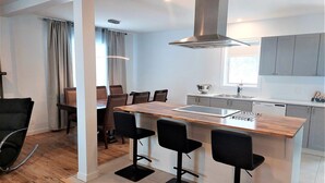 A modern kitchen with a central island, bar stools, and a dining area with chairs. - Enjoy Orleans Island at Residence Orleans with it magnificent inground pool (Sainte-Pétronille)