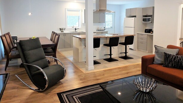A modern kitchen with white cabinets, a central island, and bar stools. - Enjoy Orleans Island at Residence Orleans with it magnificent inground pool (Sainte-Pétronille)