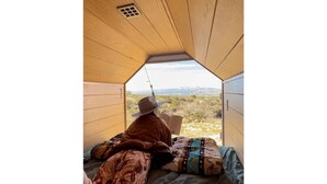 Una persona sentada en una cama dentro de una habitación tipo tienda con vistas a un paisaje.