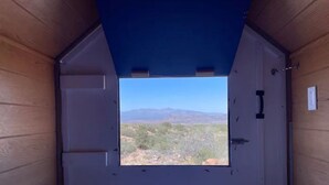 Una habitación con interior de madera y una ventana que ofrece vistas a un paisaje desértico con montañas.