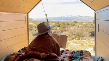 A person sitting on a bed in a tent-like room with a view of a landscape.