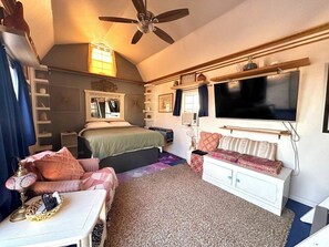 Un dormitorio acogedor con una cama, un sofá, un televisor y un ventilador de techo.