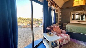A bedroom with a large window, a bed, a small table with a lamp, and a view of the outdoors. - The Eagle's Nest: Experience Arizona Agritourism (Kingman)