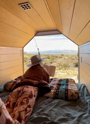 Een kamer met een bed, een persoon die een boek leest, en uitzicht op de omgeving.