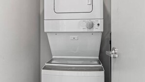 Une petite buanderie blanche, dotée d’un lave-linge et d’un sèche-linge encastrés, d’une petite fenêtre et d’une porte.