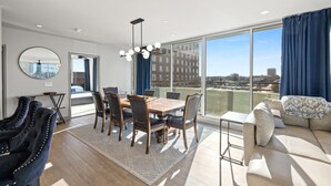 Un espace de repas moderne avec une table et des chaises en bois, un grand miroir et une vue sur la ville grâce à de grandes fenêtres.