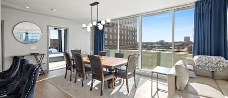 A modern dining area with a wooden table and chairs, a large mirror, and a view of the city through large windows.