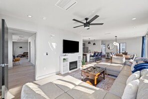 Ein modernes Wohnzimmer mit Kamin, Flachbildfernseher, Deckenventilator und Essbereich mit Barhocker.