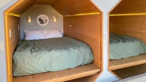 Un lit en bois de forme hexagonale, doté d’une tête de lit intégrée et de lampes fixées au mur.