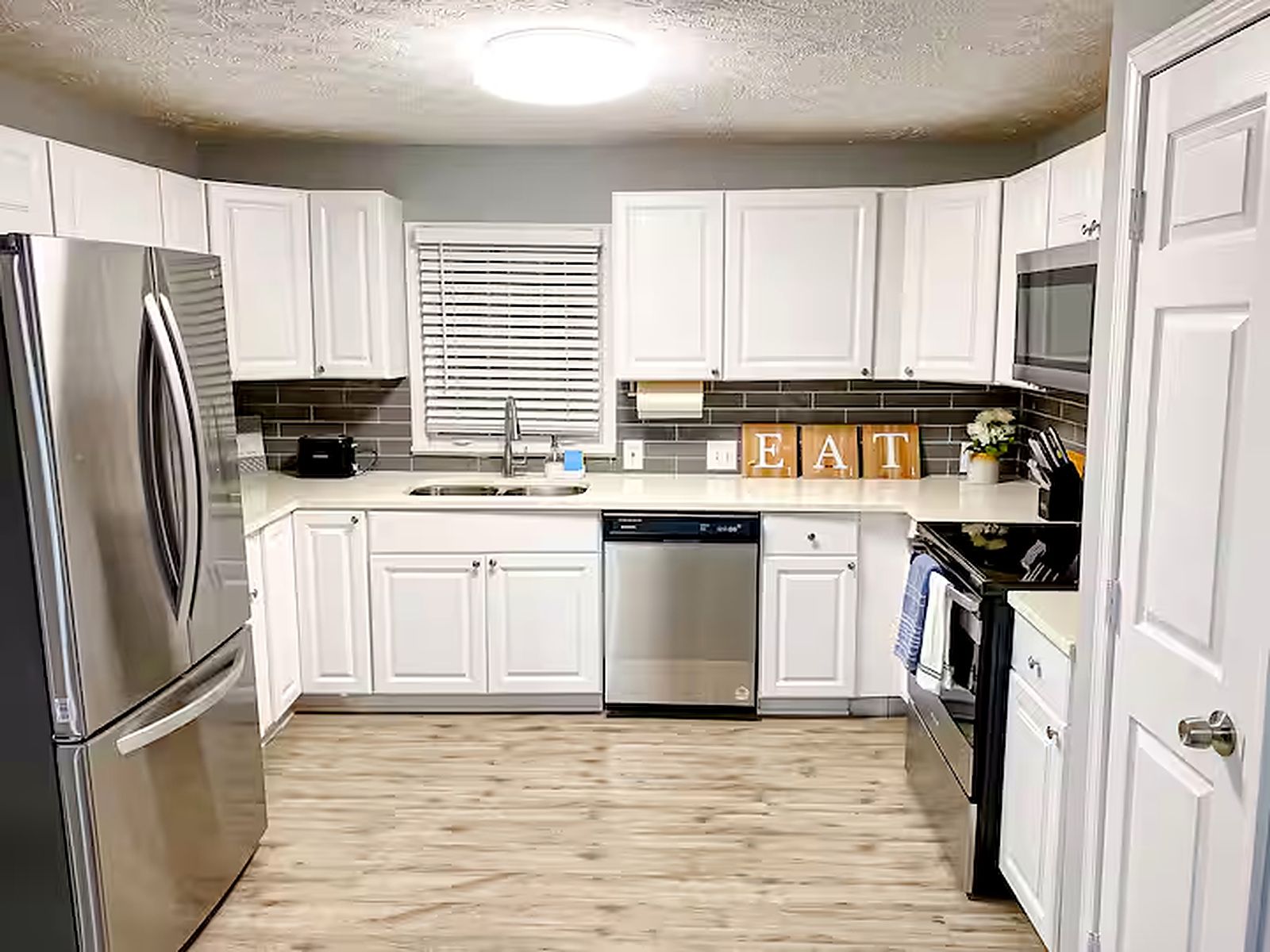 A modern kitchen with white cabinetry, a stainless steel refrigerator, a dishwasher, and a microwave.