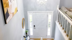 Ein Flur mit einer weißen Tür, einem Chandelier, einer Treppe und einem an der Wand hängenden, abstrakten Gemälde.