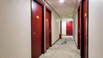 Un couloir d’hôtel avec des portes en bois, un sol recouvert de moquette et un motif décoratif sur le tapis.