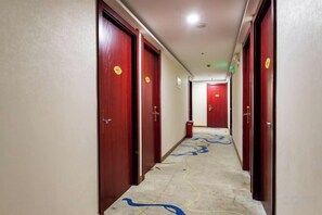 Un pasillo de hotel con puertas de madera, suelo alfombrado y un diseño de alfombra estampado.