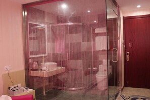 Habitación con ducha envuelta en vidrio, puerta de madera y mesita de noche con teléfono.