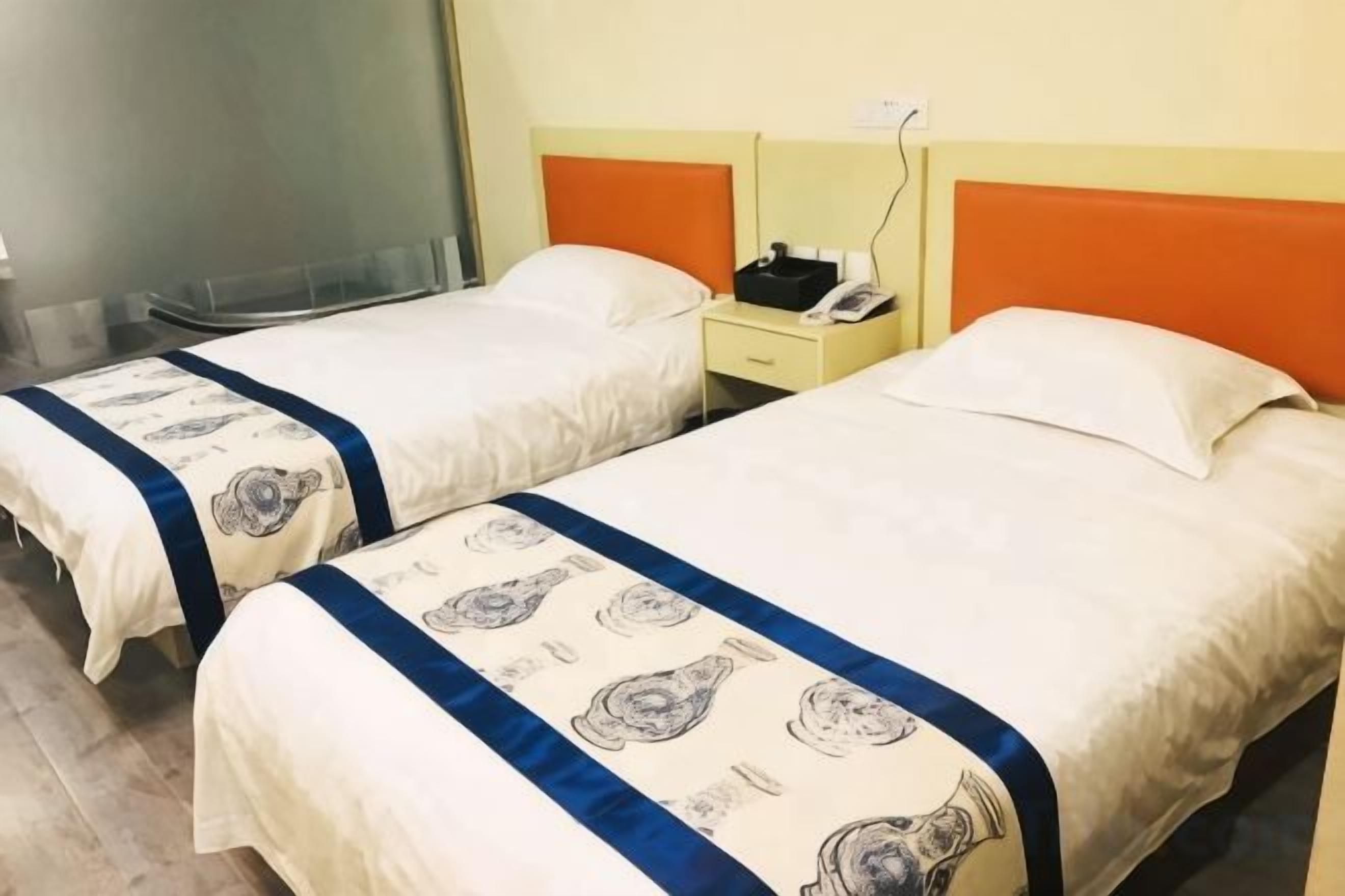 Duas camas de casal com cabeceiras e mesas de cabeceira combinando, cada uma com uma luminária e um telefone.