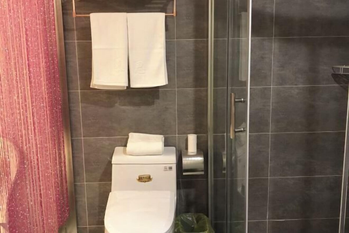 Un baño con inodoro, toallero con dos toallas, dispensador de toallas de papel y un cesto de basura.