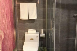 Un baño con inodoro, toallero con dos toallas, dispensador de toallas de papel y un cesto de basura.
