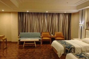 A hotel room with a bed, two armchairs, a sofa, a small table, and a large curtain.