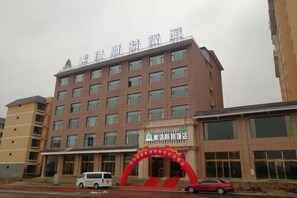 A multi-story hotel with a red archway entrance, a sign indicating a business center, and a parking area with vehicles.