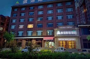 Un hotel de varios pisos con una fila de ventanas en cada planta, una entrada a nivel de calle con un letrero y un área de estacionamiento al frente.