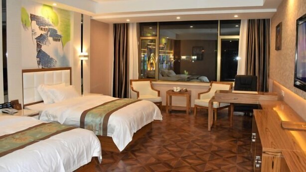 A hotel room with two beds, a desk, a chair, a TV, and a large window.