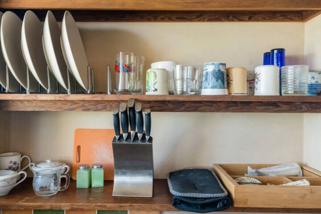 A kitchen with wooden shelves holding plates, cups, and a knife block.