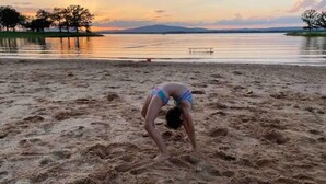 Een persoon maakt een yoga-houding op een zandstrand, met een zonsondergang op de achtergrond.