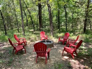 Relax in a serene forest setting with a fire pit and Adirondack chairs.