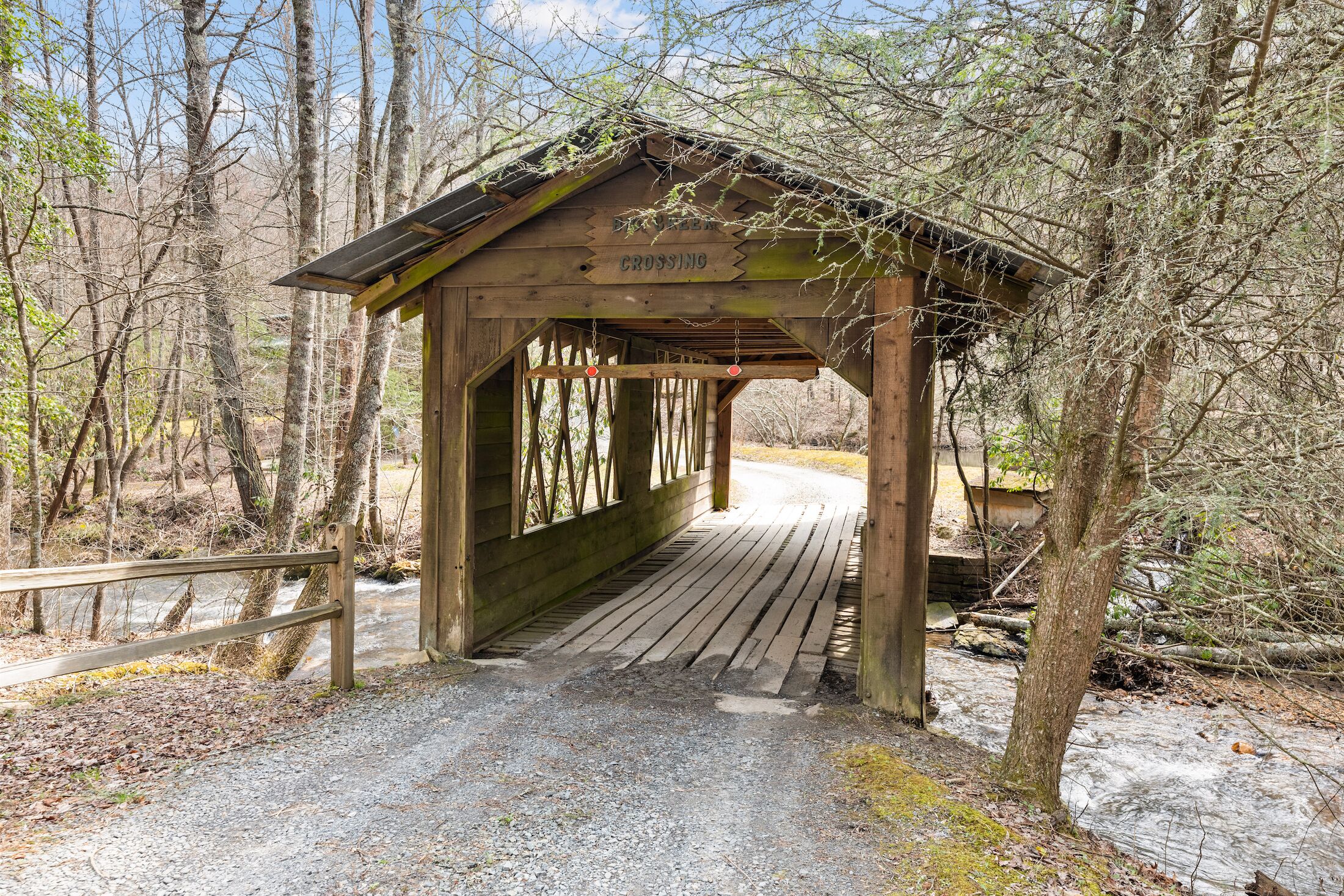 A wooden covered bridge with a sign reading "Crossing" in a wooded area.