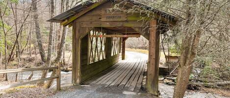 A wooden covered bridge with a sign reading "Crossing" in a wooded area.