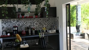 A modern kitchen with a central island, red stools, hanging plants, and a view of the outdoor patio. - splendid villa with its infinity pool offering you a view of nature (Las Terrenas)