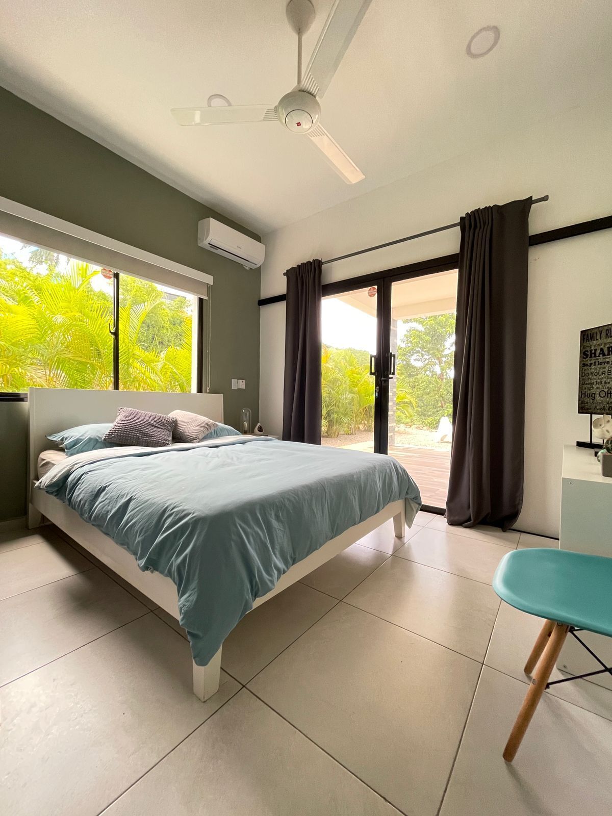 Une chambre avec un lit, un bureau, un ventilateur de plafond et une vue sur la verdure.