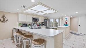 Una cocina moderna con una isla central, muebles blancos y un ventanal grande.