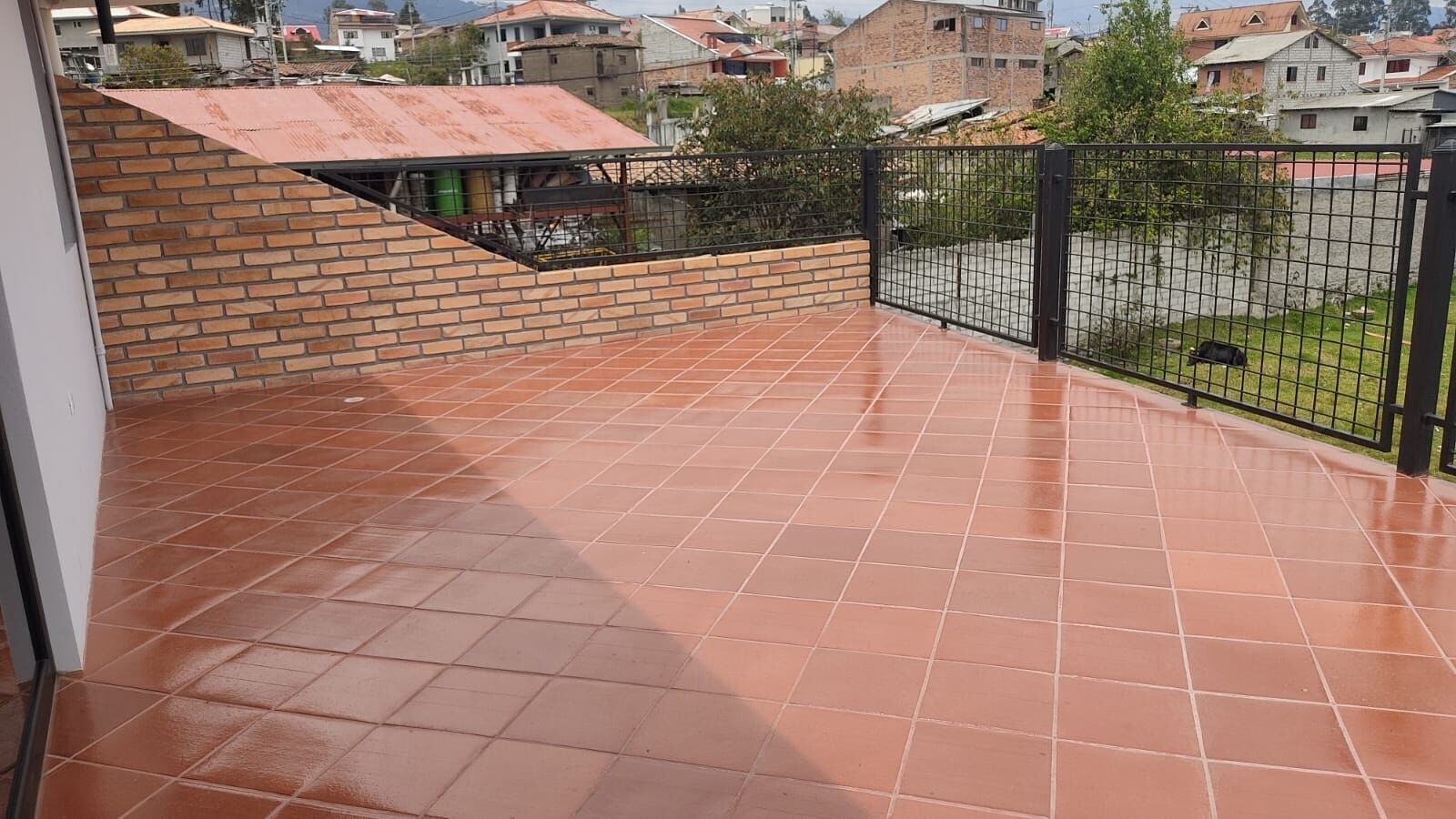 A balcony with terracotta tiles, a brick wall, and a metal fence.
