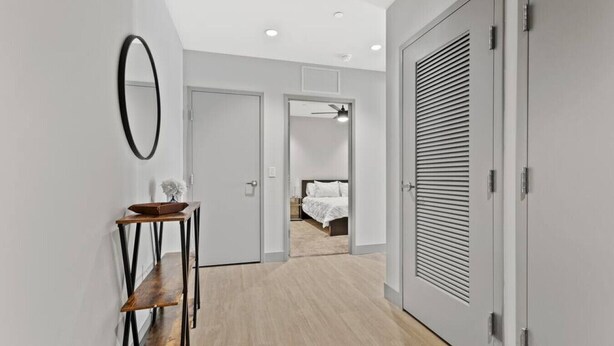 A hallway with a wooden floor, a mirror, a small table with a vase, and a bed in the background. - 175 LEX - Spacious Two Bedroom! Walkable Downtown! (Lexington)